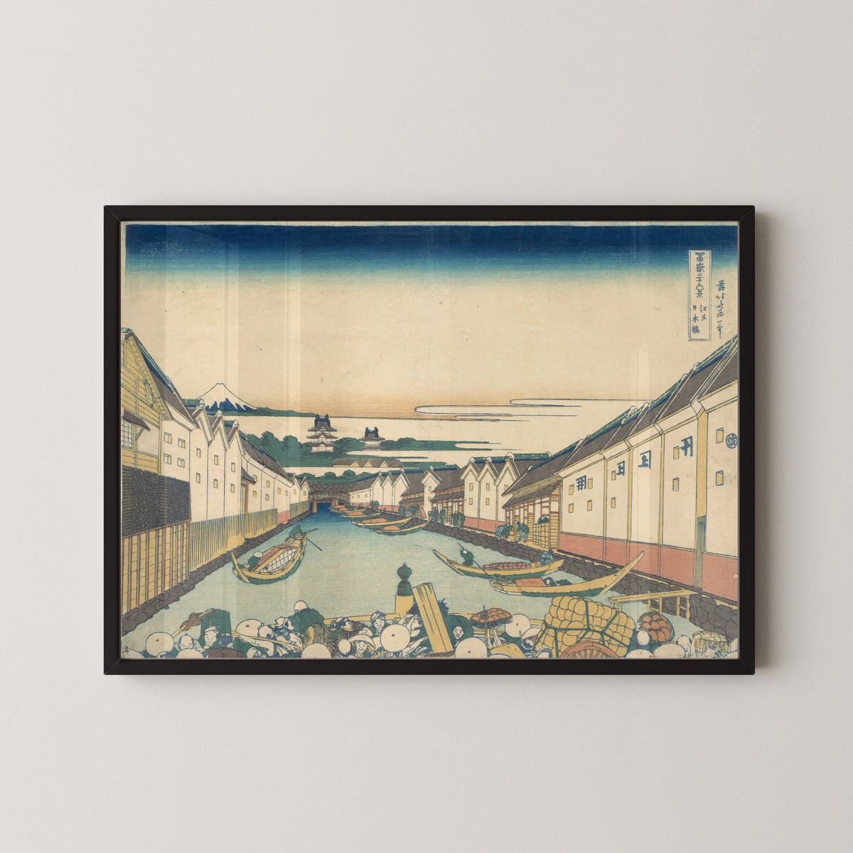 Framed art print of Thirty-six Views of Mount Fuji: Nihonbashi in Edo by Katsushika Hokusai, in a black frame on a pale wall