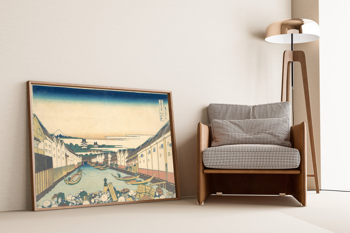 Framed art print of Thirty-six Views of Mount Fuji: Nihonbashi in Edo by Katsushika Hokusai, leaning against a wall beside an armchair and a floor lamp