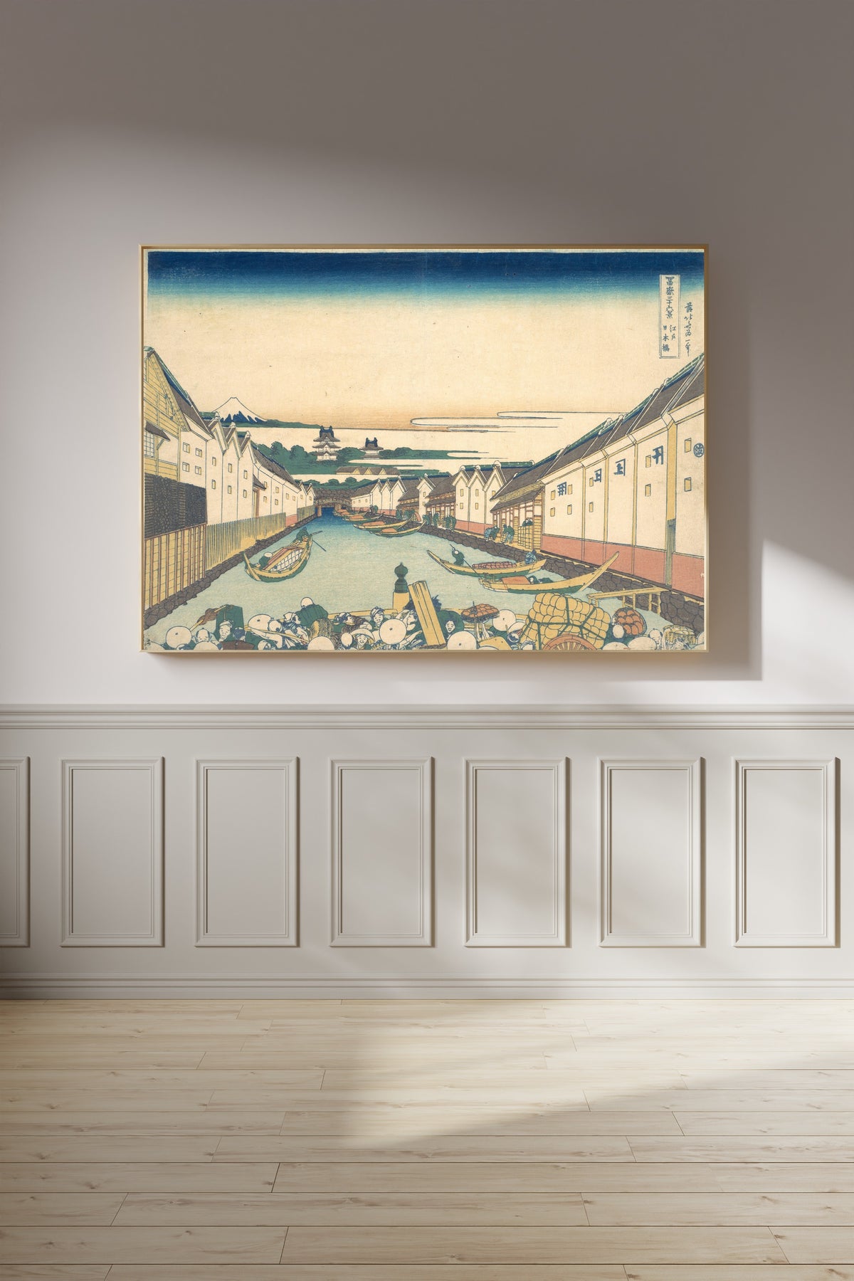 Framed art print of Thirty-six Views of Mount Fuji: Nihonbashi in Edo by Katsushika Hokusai, on a panelled wall in afternoon light