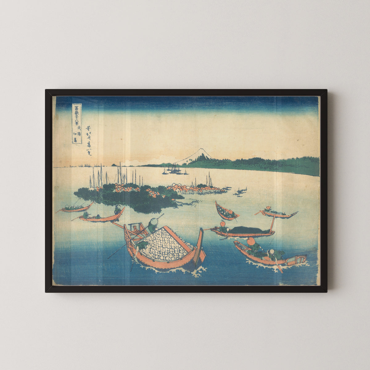 Framed art print of Thirty-six Views of Mount Fuji: Tsukudajima in Musashi Province by Katsushika Hokusai, in a black frame on a pale wall