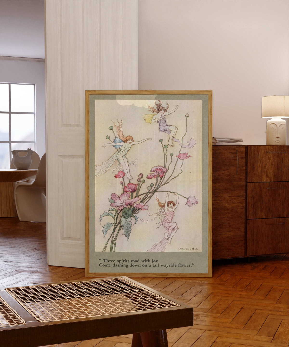 Framed art print of Three spirits mad with joy come dashing down on a tall… by Warwick Goble, in a light wood frame leaning in a warm room with a parquet floor