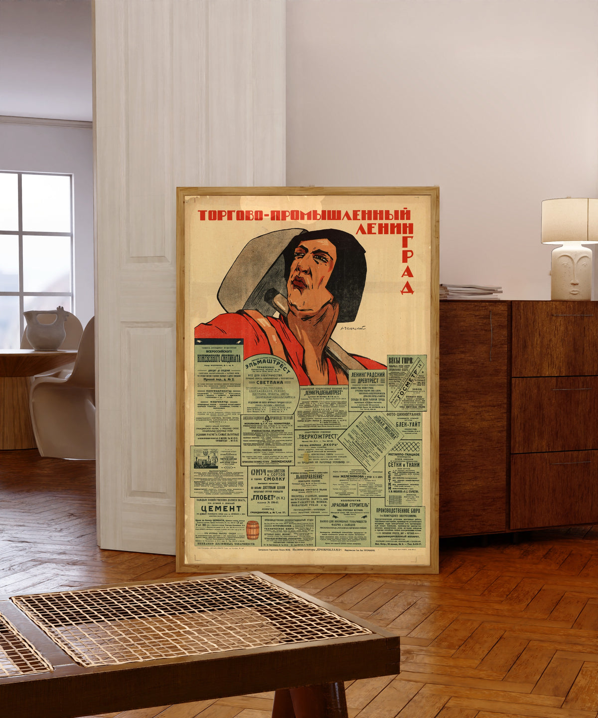 Framed art print of Trade and Industrial Leningrad by Alexander Zelensky, in a light wood frame leaning in a warm room with a parquet floor