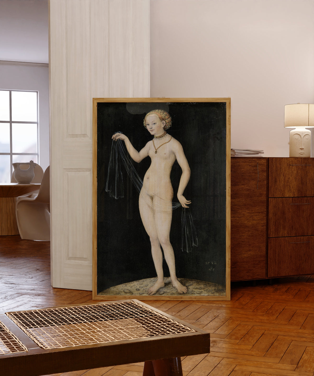 Framed art print of Venus by Lucas Cranach the Elder, in a light wood frame leaning in a warm room with a parquet floor