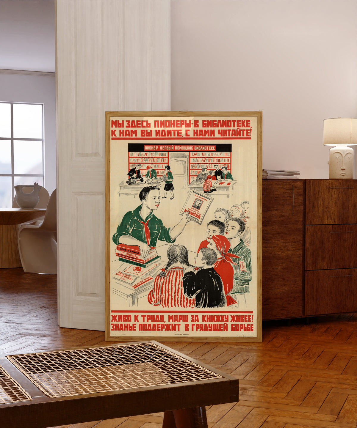 Framed art print of We pioneers are here in the library: come to us, read with us!, in a light wood frame leaning in a warm room with a parquet floor