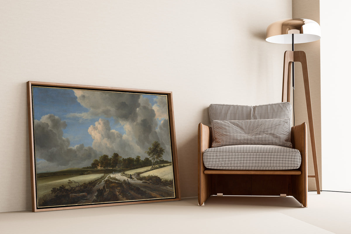 Wheat Fields by Jacob van Ruisdael — framed and leaning against a wall beside an armchair and a floor lamp