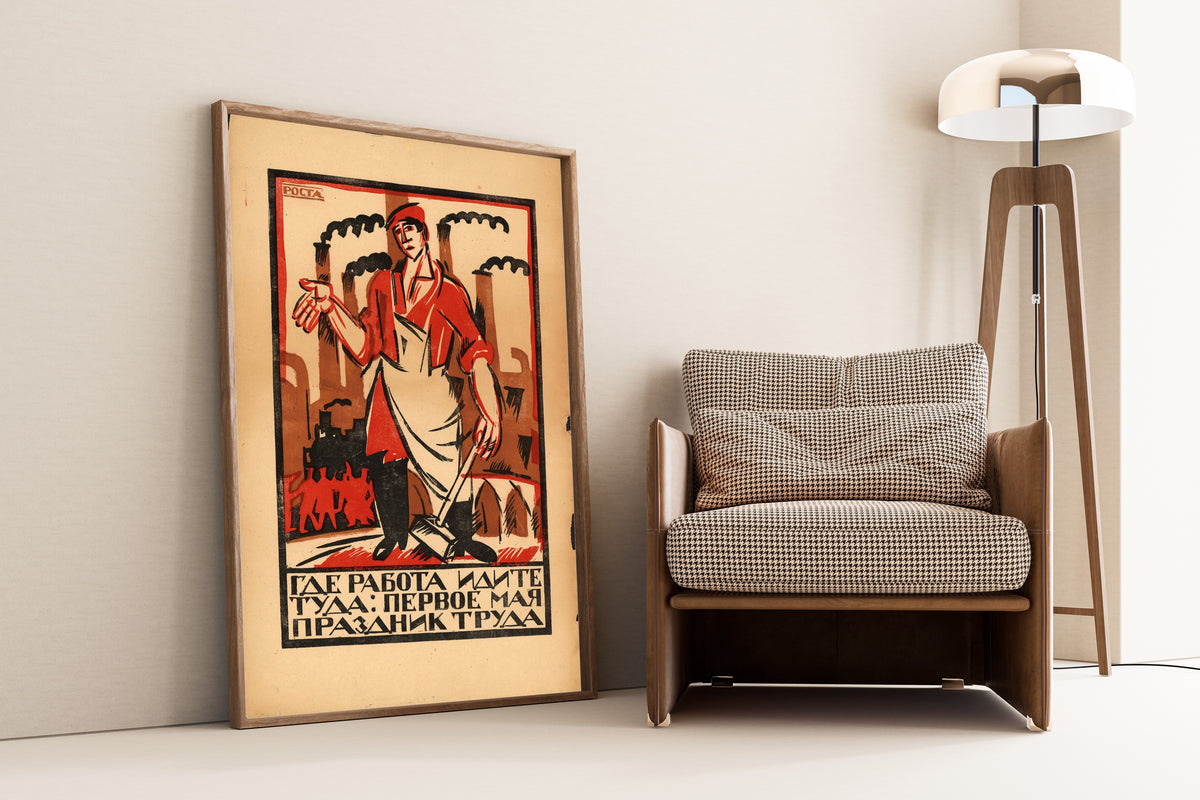 Framed art print of Where There Is Work, Go There: May Day Is the Holiday of Labour by Ivan Malyutin, leaning against a wall beside an armchair and a floor lamp