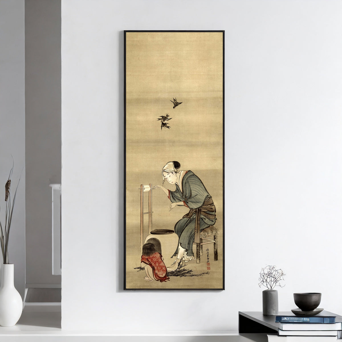 Framed art print of Woman Spinning Silk by Katsushika Hokusai, on a white wall above books and a bowl