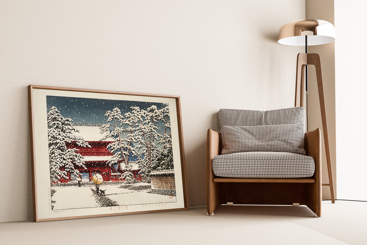 Framed art print of Zojoji Temple in Snow by Kawase Hasui, leaning against a wall beside an armchair and a floor lamp