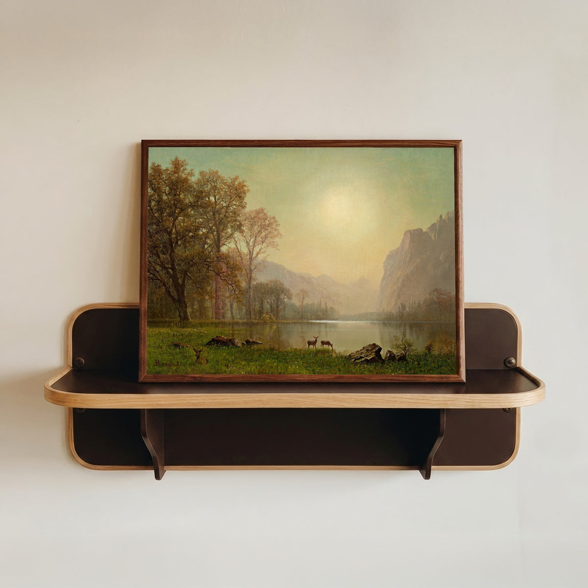 Framed art print of Dawn in the Rockies by Albert Bierstadt, in a dark wood frame resting on a wall shelf