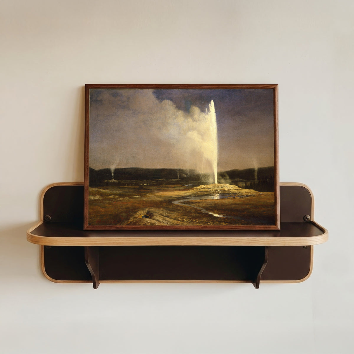 Framed art print of Geysers by Albert Bierstadt, in a dark wood frame resting on a wall shelf