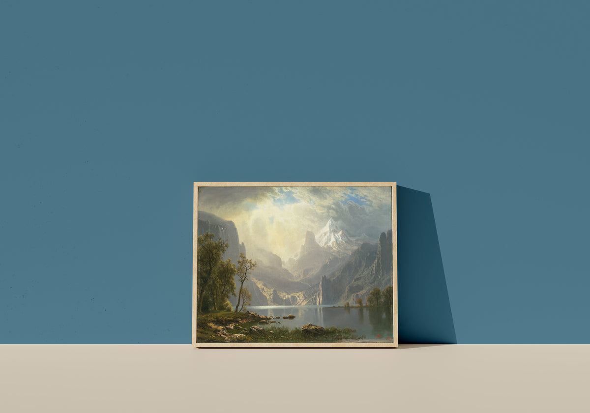 Framed art print of In the Sierras by Albert Bierstadt, in a light wood frame leaning on a blue wall