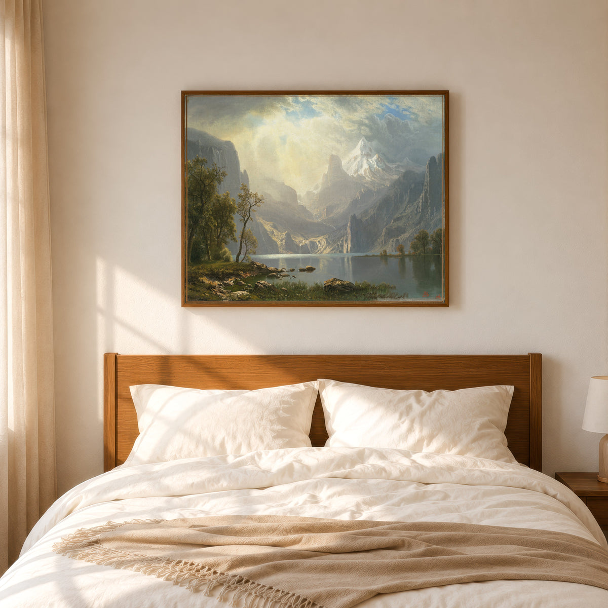 Framed art print of In the Sierras by Albert Bierstadt, in a slim wood frame above a bed in a sunlit bedroom