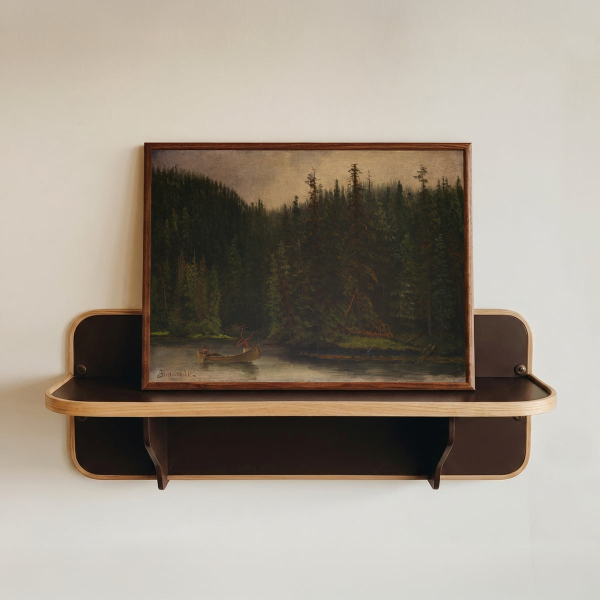 Framed art print of Indian Hunters in Canoe by Albert Bierstadt, in a dark wood frame resting on a wall shelf