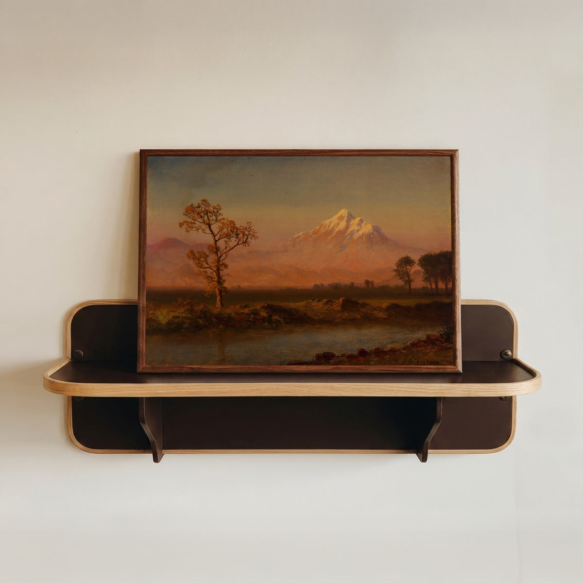 Framed art print of Mount Hood by Albert Bierstadt, in a dark wood frame resting on a wall shelf