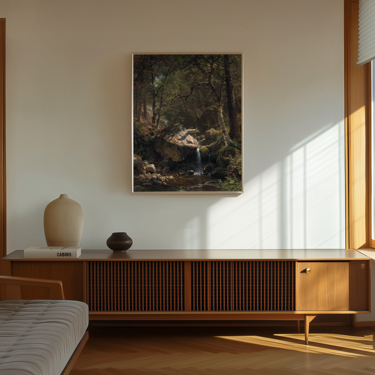 Framed art print of Mountain Brook by Albert Bierstadt, in a thin light frame on a sunlit wall above a wooden sideboard