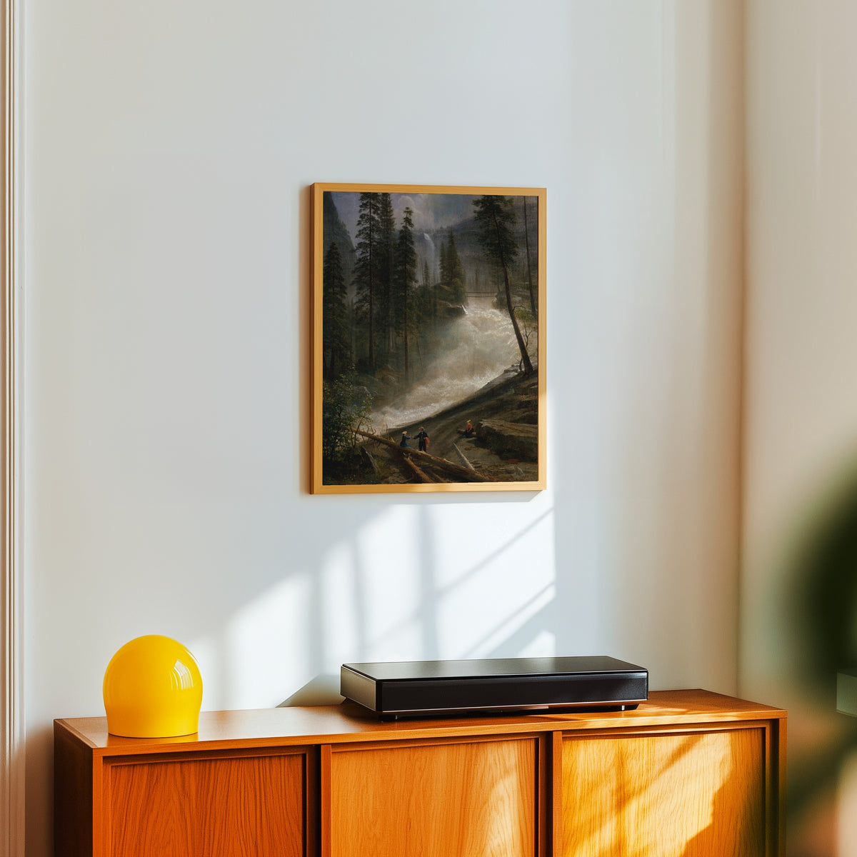 Framed art print of Nevada Falls, Yosemite by Albert Bierstadt, in a light wood frame on a white wall above an orange sideboard