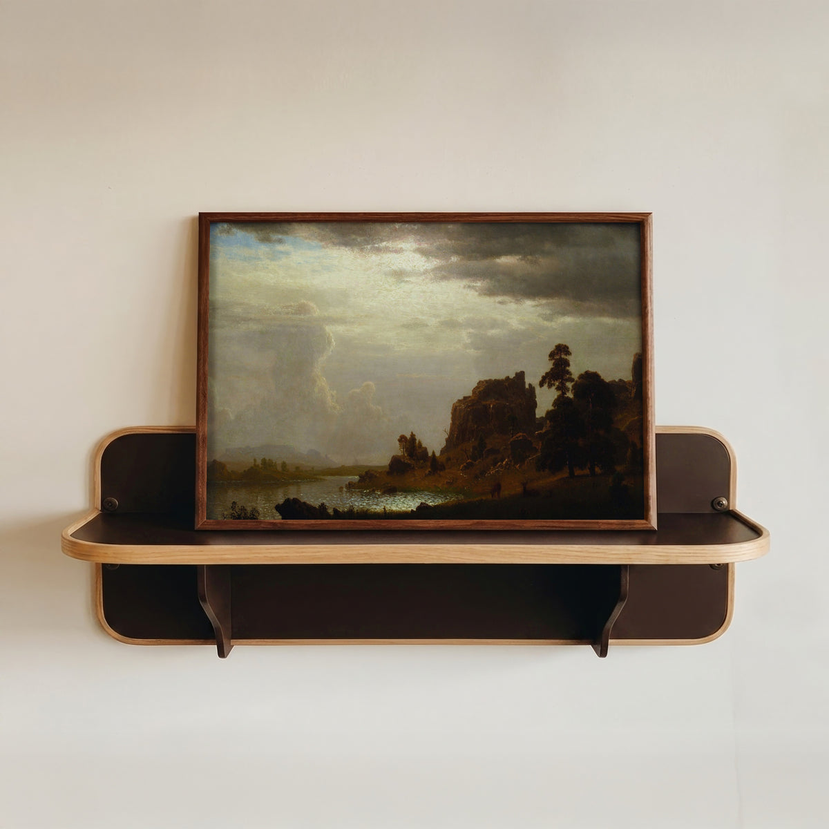 Framed art print of On the Sweetwater near the Devil's Gate by Albert Bierstadt, in a dark wood frame resting on a wall shelf