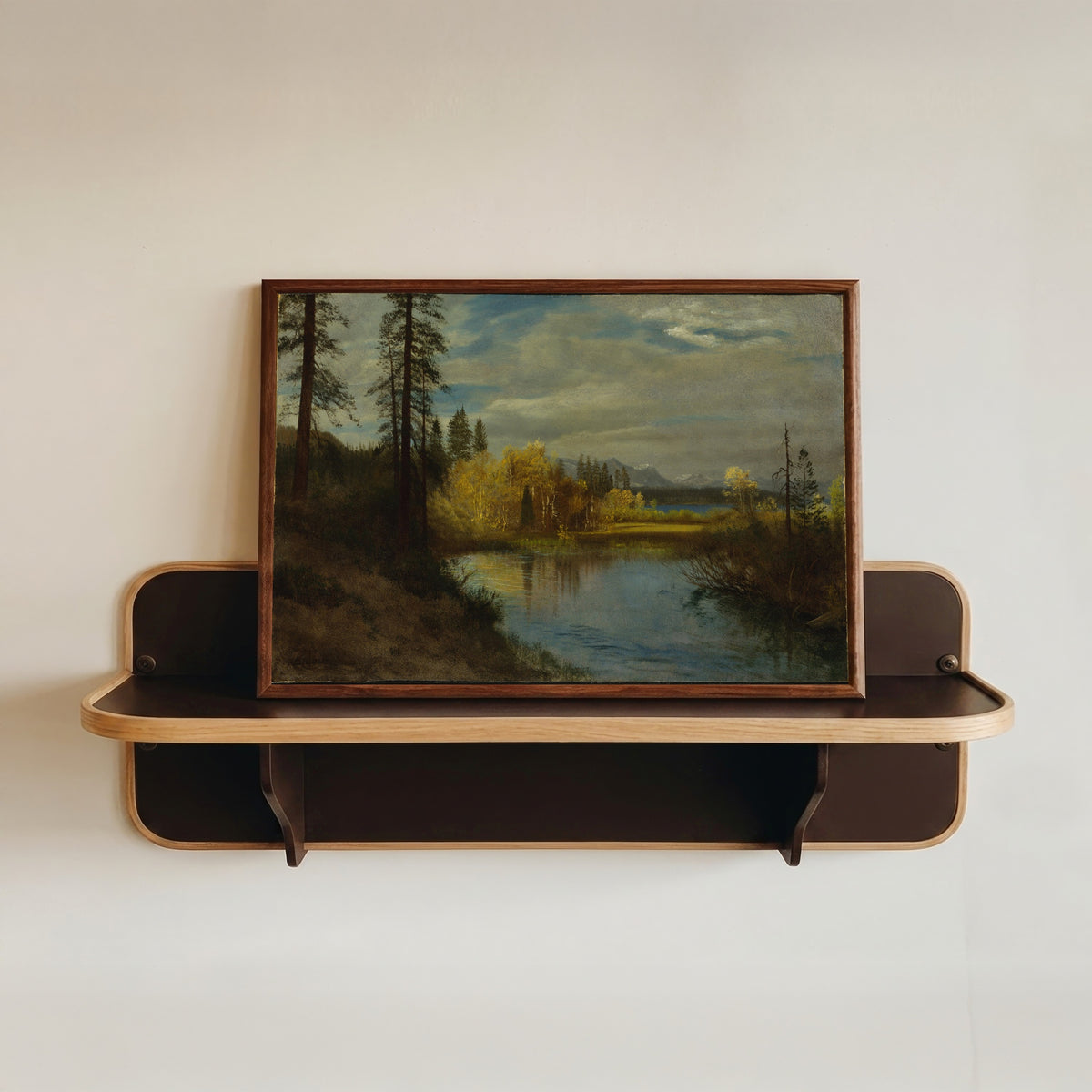 Framed art print of Outlet at Lake Tahoe by Albert Bierstadt, in a dark wood frame resting on a wall shelf