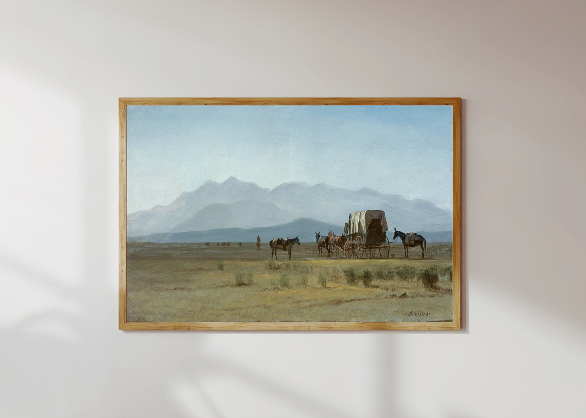 Framed art print of Surveyor's Wagon in the Rockies by Albert Bierstadt, in a light wood frame on a sunlit white wall