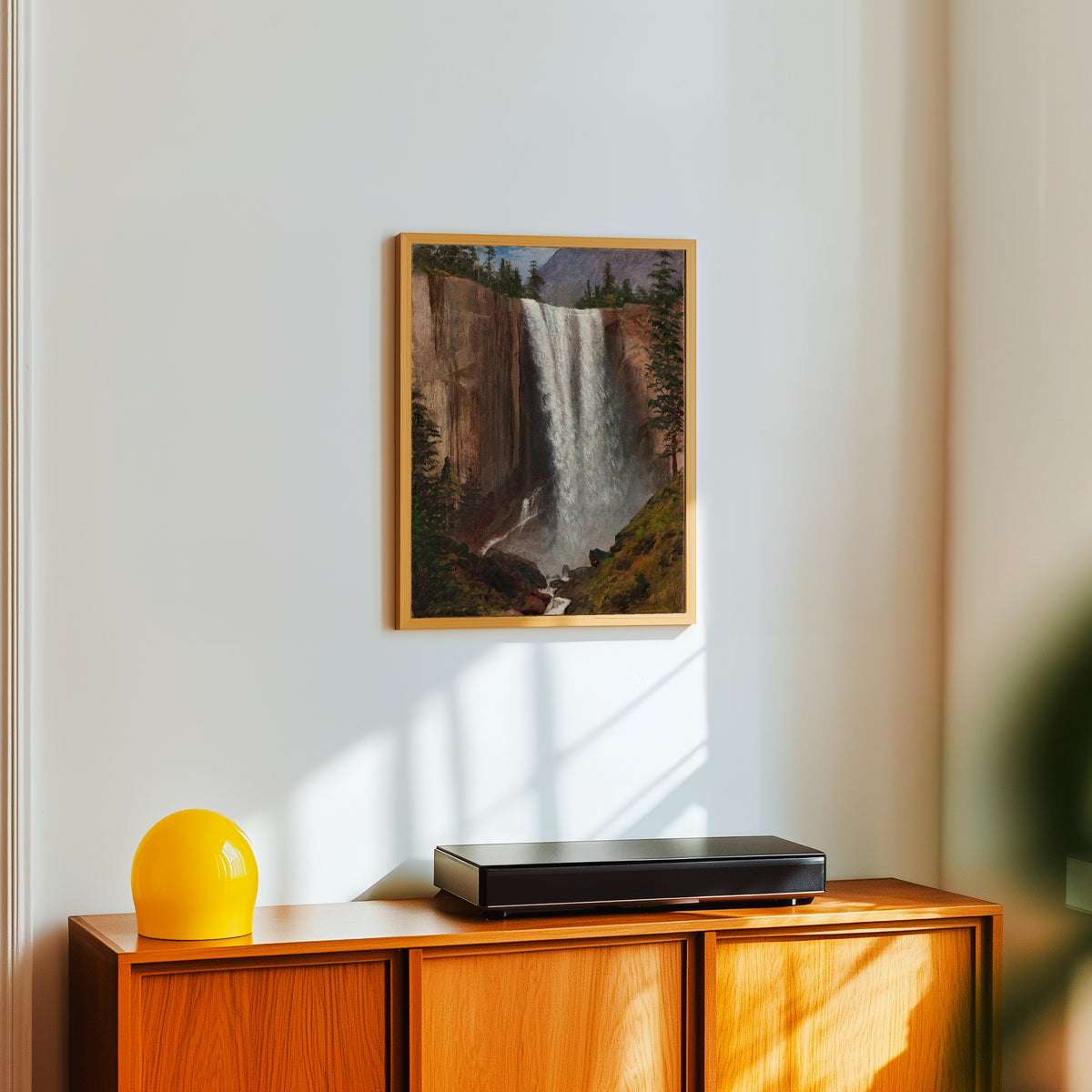 Framed art print of Vernal Fall by Albert Bierstadt, in a light wood frame on a white wall above an orange sideboard