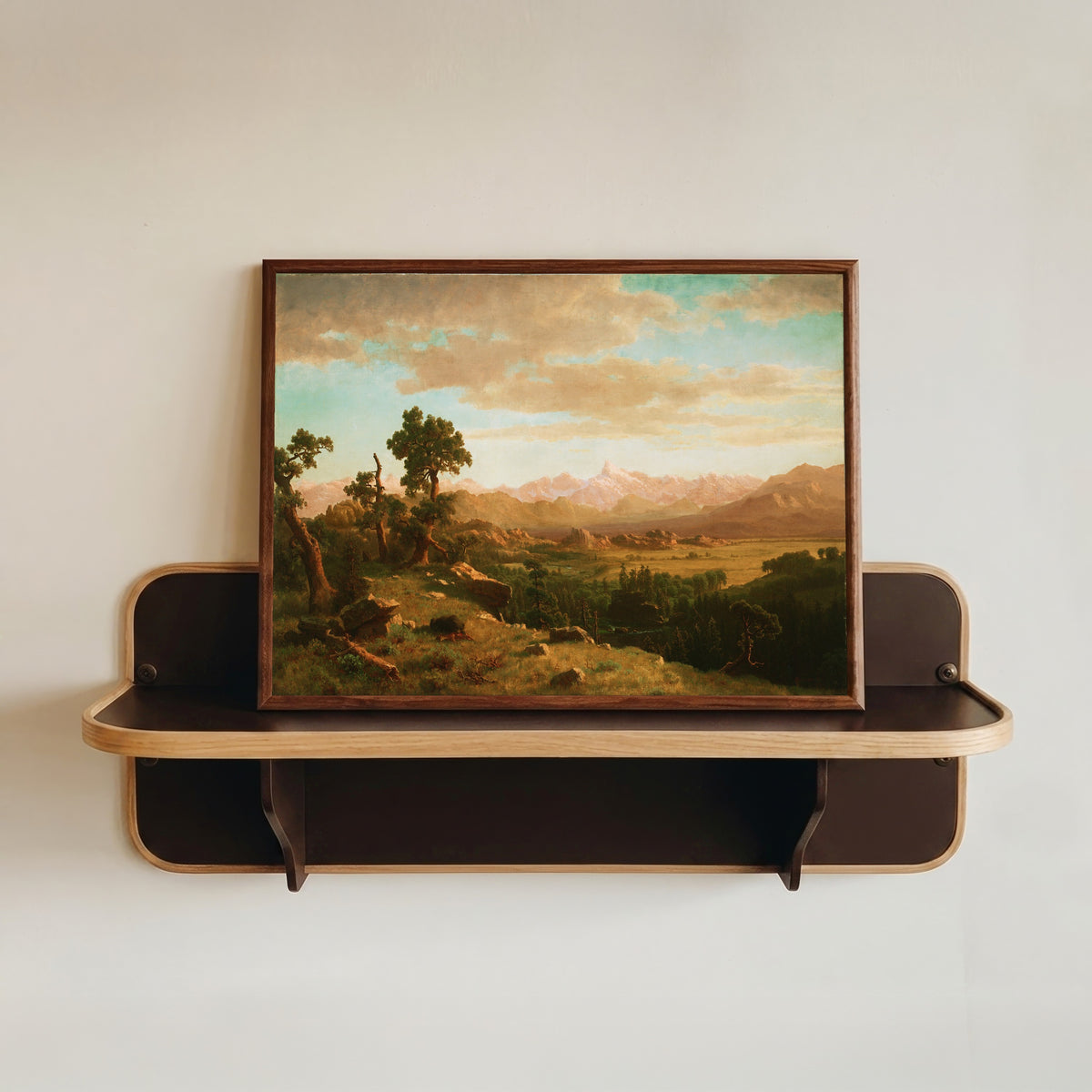 Framed art print of Wind River Country by Albert Bierstadt, in a dark wood frame resting on a wall shelf
