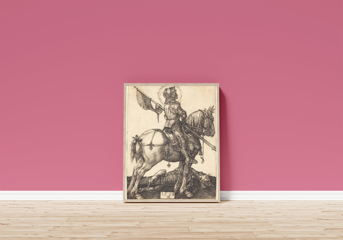 Framed art print of Saint George on Horseback by Albrecht Dürer, in a light wood frame leaning on a pink wall above a wooden floor