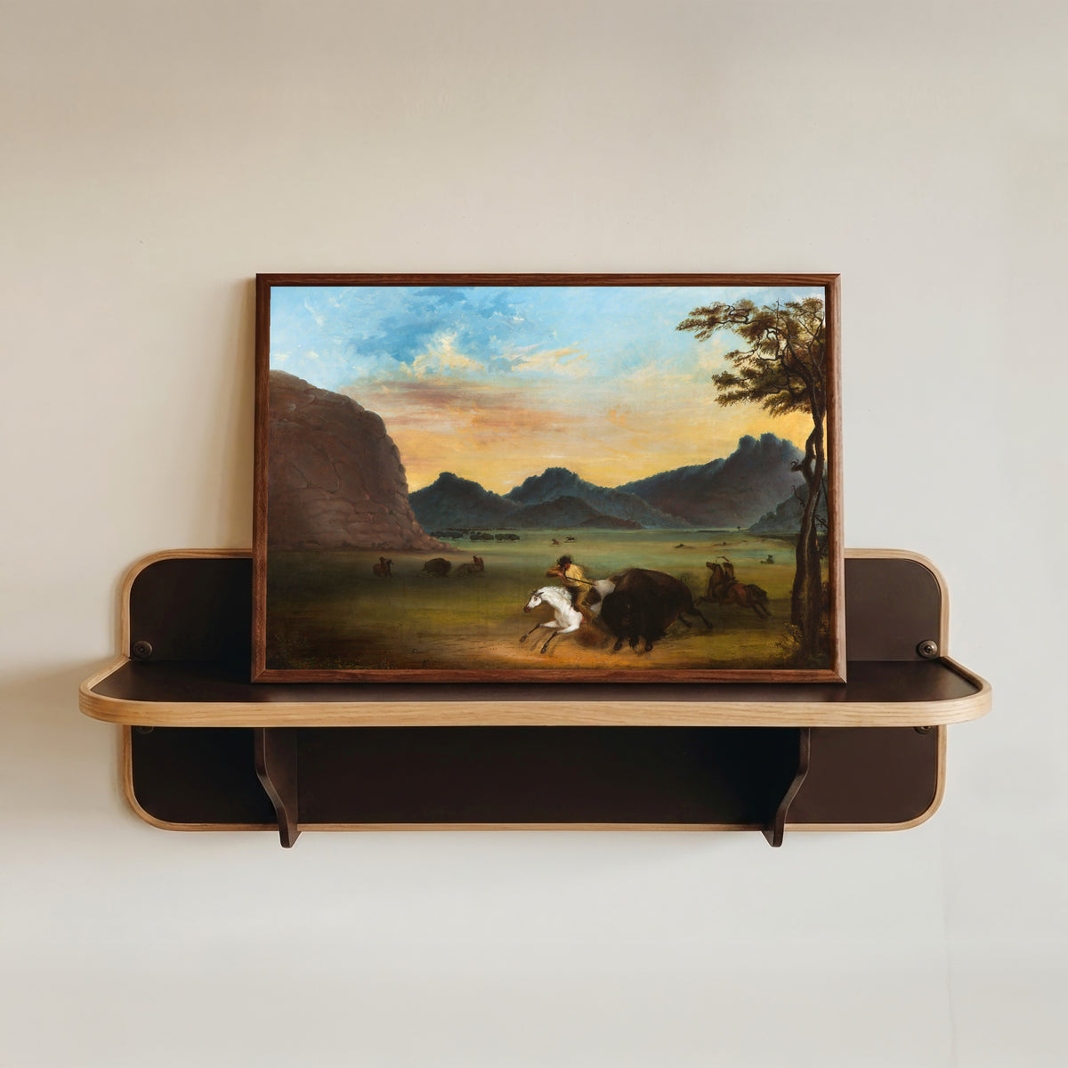 Framed art print of Buffalo Hunt by Alfred Jacob Miller, in a dark wood frame resting on a wall shelf