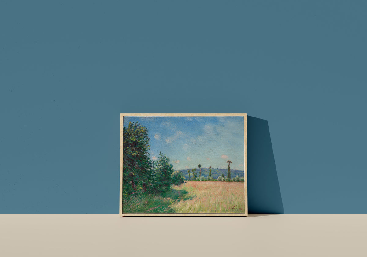 Framed art print of Sahurs Meadows in Morning Sun by Alfred Sisley, in a light wood frame leaning on a blue wall