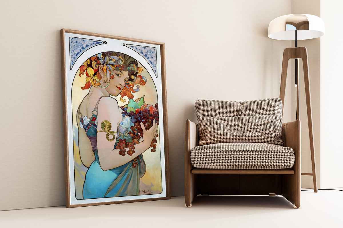 Framed art print of Fruit by Alphonse Mucha, leaning against a wall beside an armchair and a floor lamp