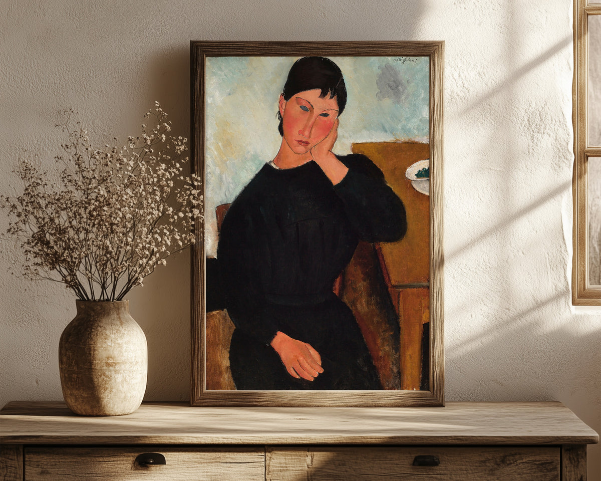 Framed art print of Elvira Resting at a Table by Amedeo Modigliani, in a dark wood frame leaning on a rustic console beside dried flowers