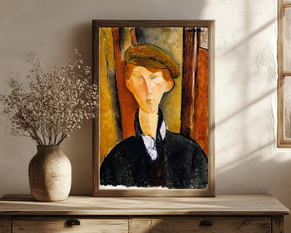 Framed art print of Young Man with a Cap by Amedeo Modigliani, in a dark wood frame leaning on a rustic console beside dried flowers