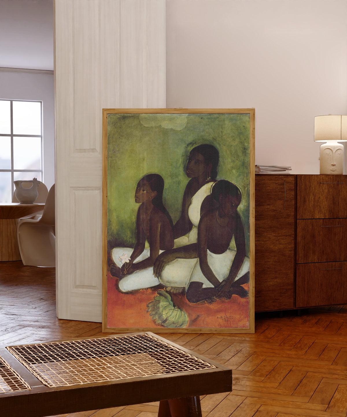 Framed art print of Fruit Vendors (1937) by Amrita Sher-Gil, in a light wood frame leaning in a warm room with a parquet floor