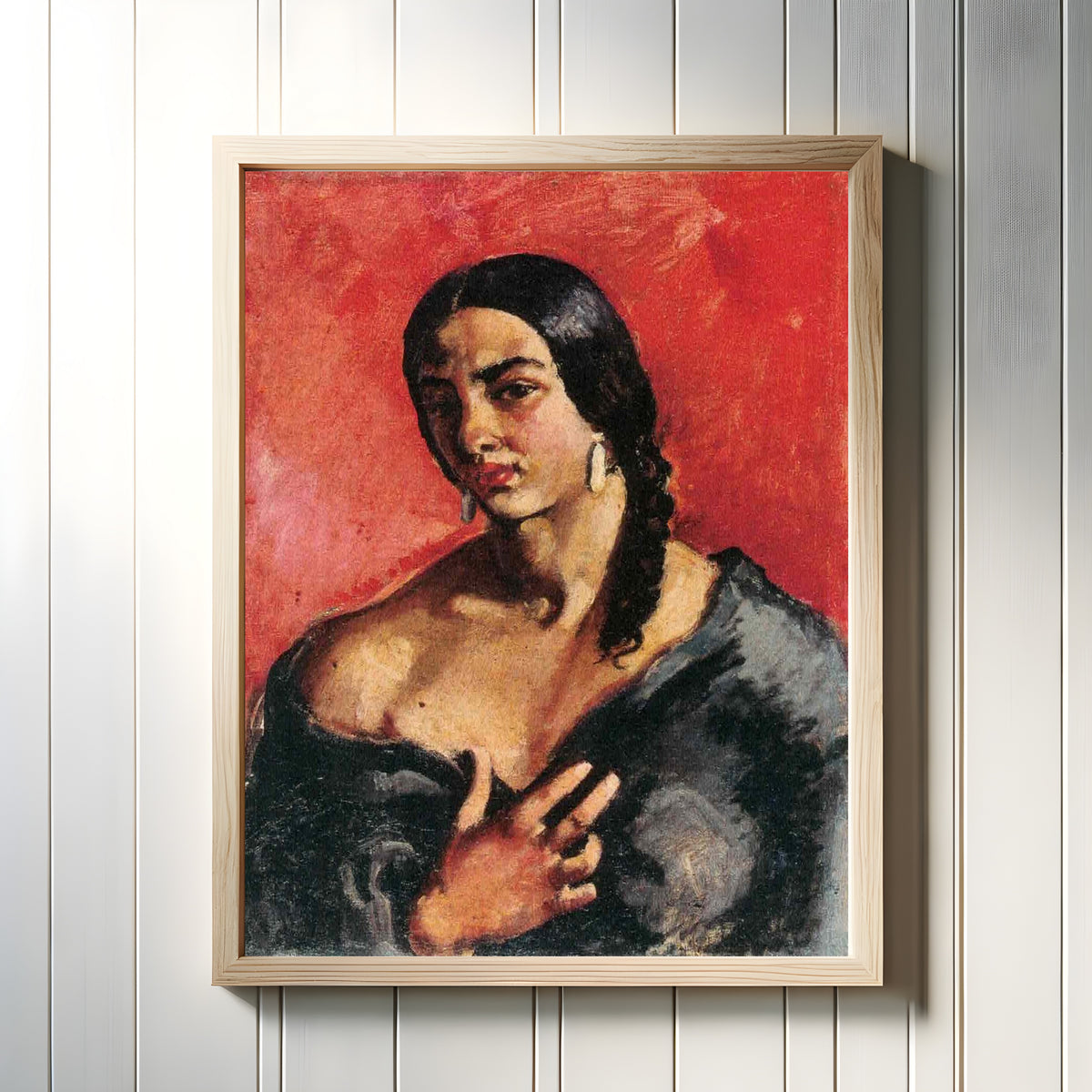 Framed art print of Self-Portrait with Red Background (c. 1930) by Amrita Sher-Gil, in a light wood frame on a white panelled wall