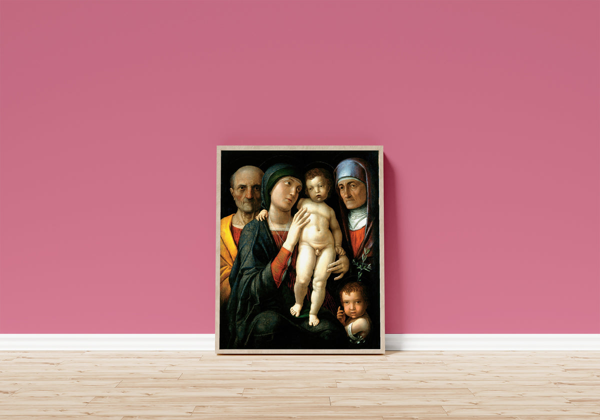 Framed art print of The Holy Family by Andrea Mantegna, in a light wood frame leaning on a pink wall above a wooden floor