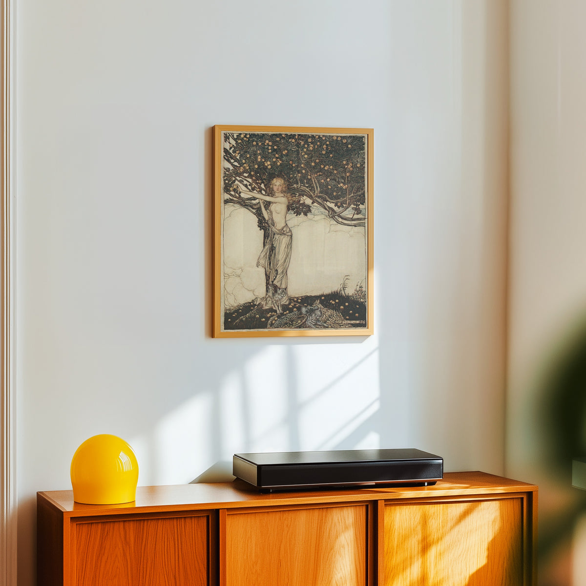 Framed art print of Freia, the Fair One by Arthur Rackham, in a light wood frame on a white wall above an orange sideboard
