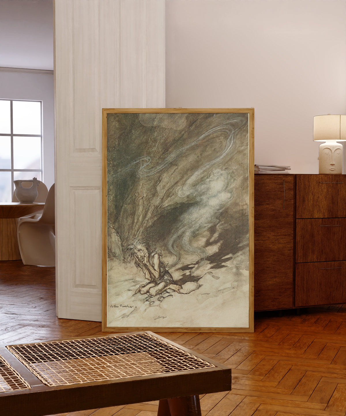 Framed art print of Mime Writhes Under the Lashes He Receives by Arthur Rackham, in a light wood frame leaning in a warm room with a parquet floor