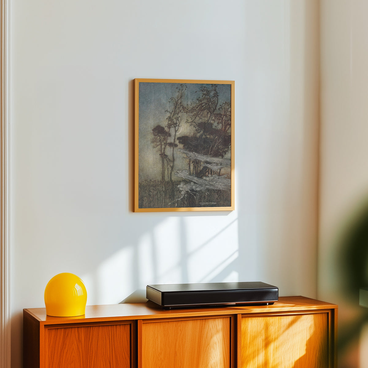 Framed art print of The Moon, Like to a Silver Bow New-Bent in Heaven by Arthur Rackham, in a light wood frame on a white wall above an orange sideboard