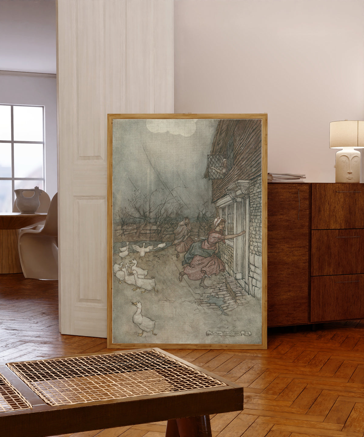 Framed art print of The Rain Always Made a Point of Setting In by Arthur Rackham, in a light wood frame leaning in a warm room with a parquet floor