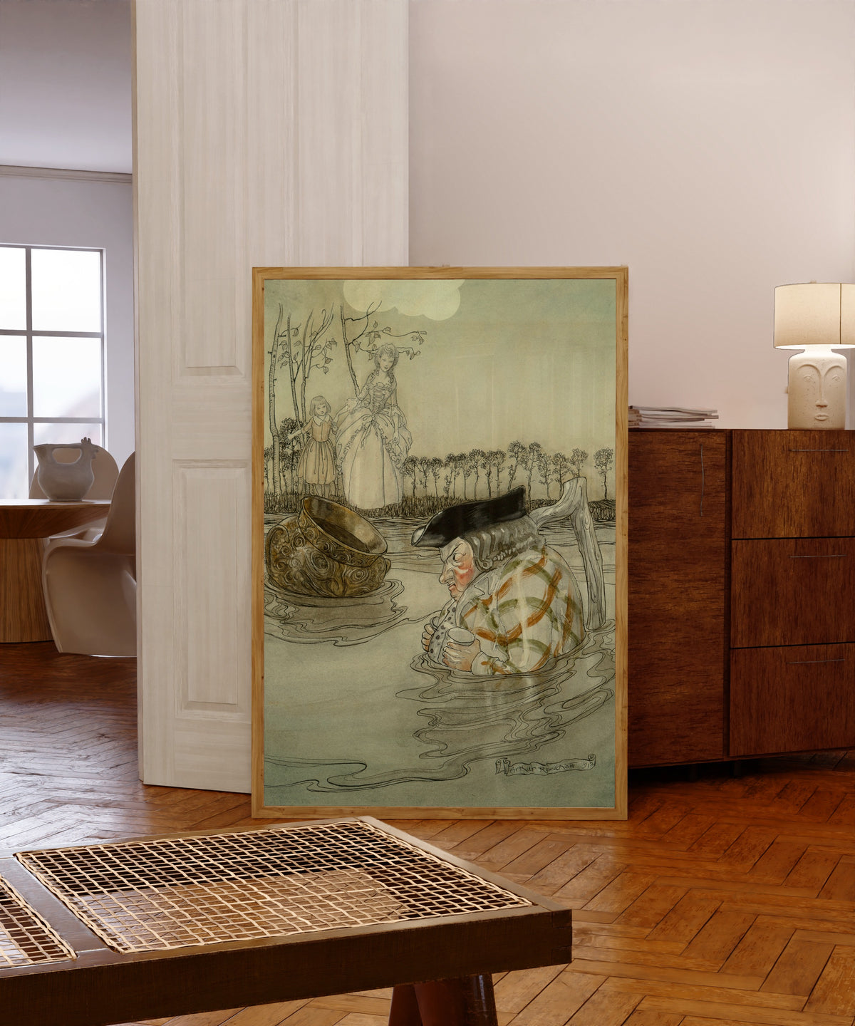 Framed art print of The Two Pots by Arthur Rackham, in a light wood frame leaning in a warm room with a parquet floor