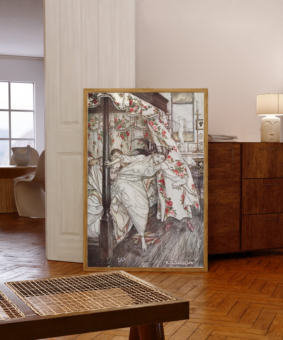 Framed art print of Venus and the Cat by Arthur Rackham, in a light wood frame leaning in a warm room with a parquet floor