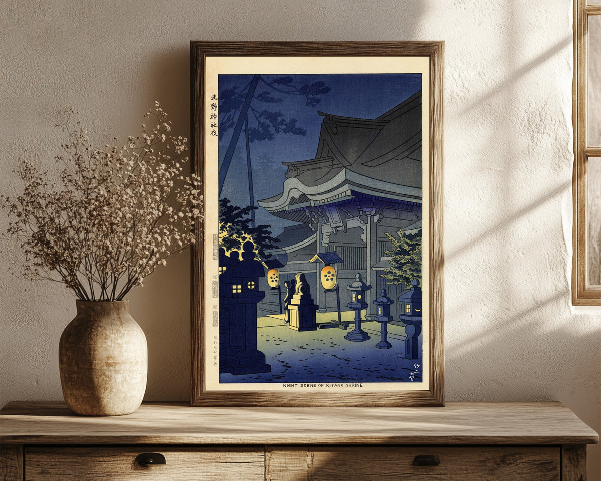 Framed art print of Night Scene of Kitano Shrine by Asano Takeji, in a dark wood frame leaning on a rustic console beside dried flowers