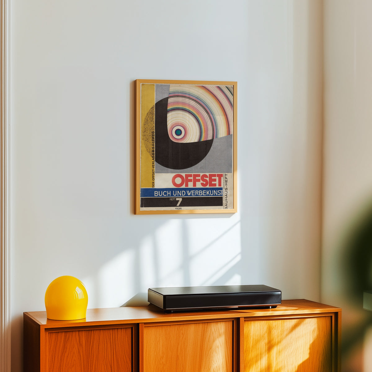 Framed art print of Bauhaus Offset Magazine Cover by Joost Schmidt, in a light wood frame on a white wall above an orange sideboard