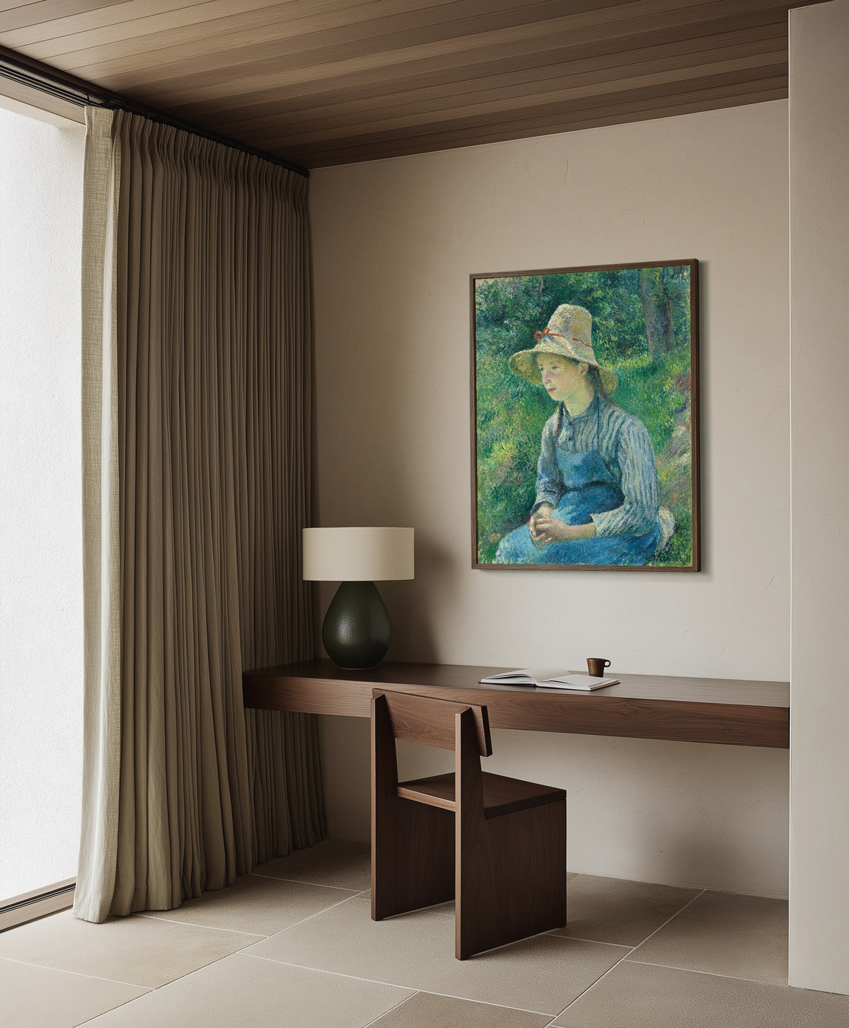 Framed art print of Peasant Girl with a Straw Hat by Camille Pissarro, in a dark wood frame on a plaster wall above a walnut desk