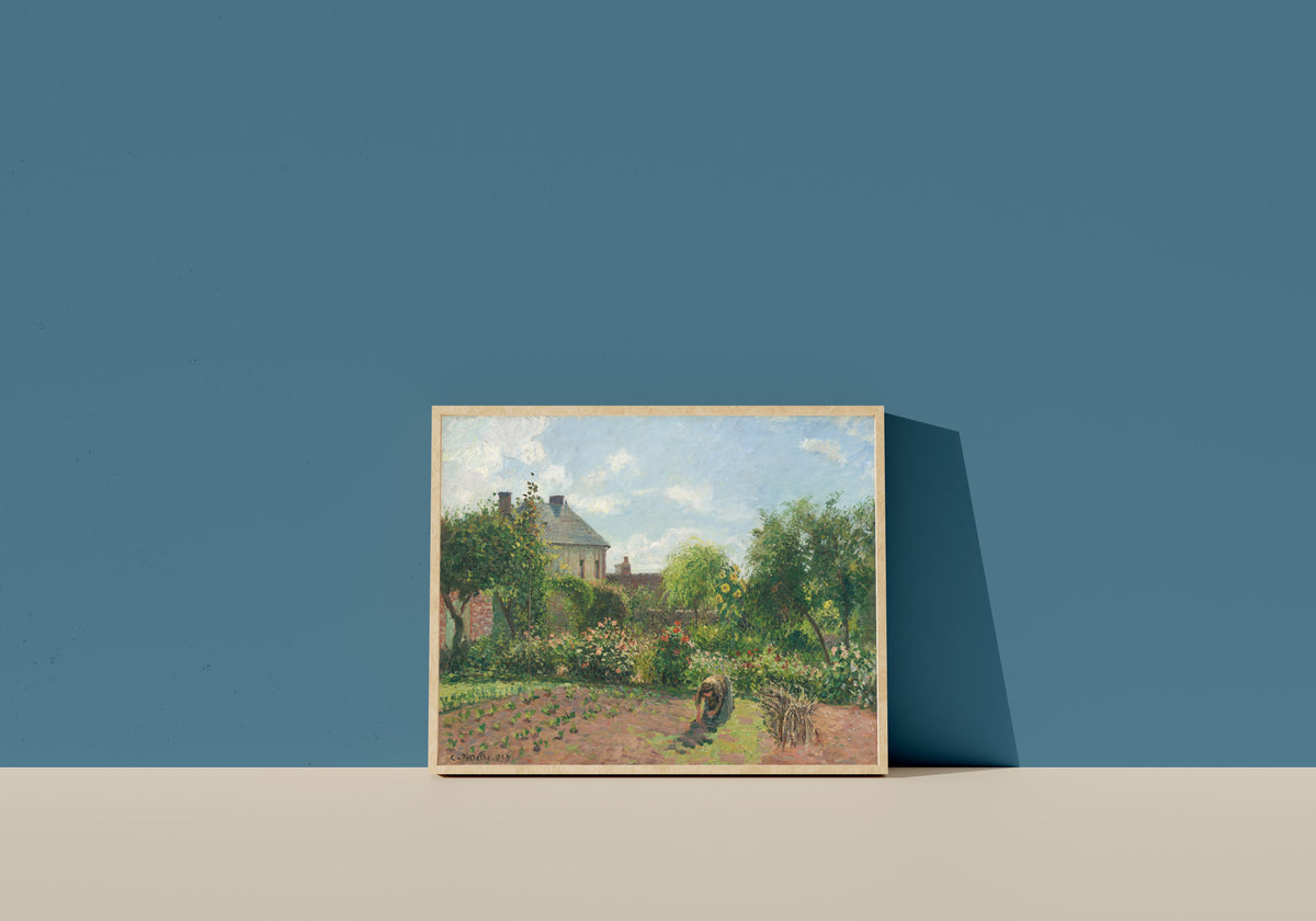 Framed art print of The Artist's Garden at Eragny by Camille Pissarro, in a light wood frame leaning on a blue wall