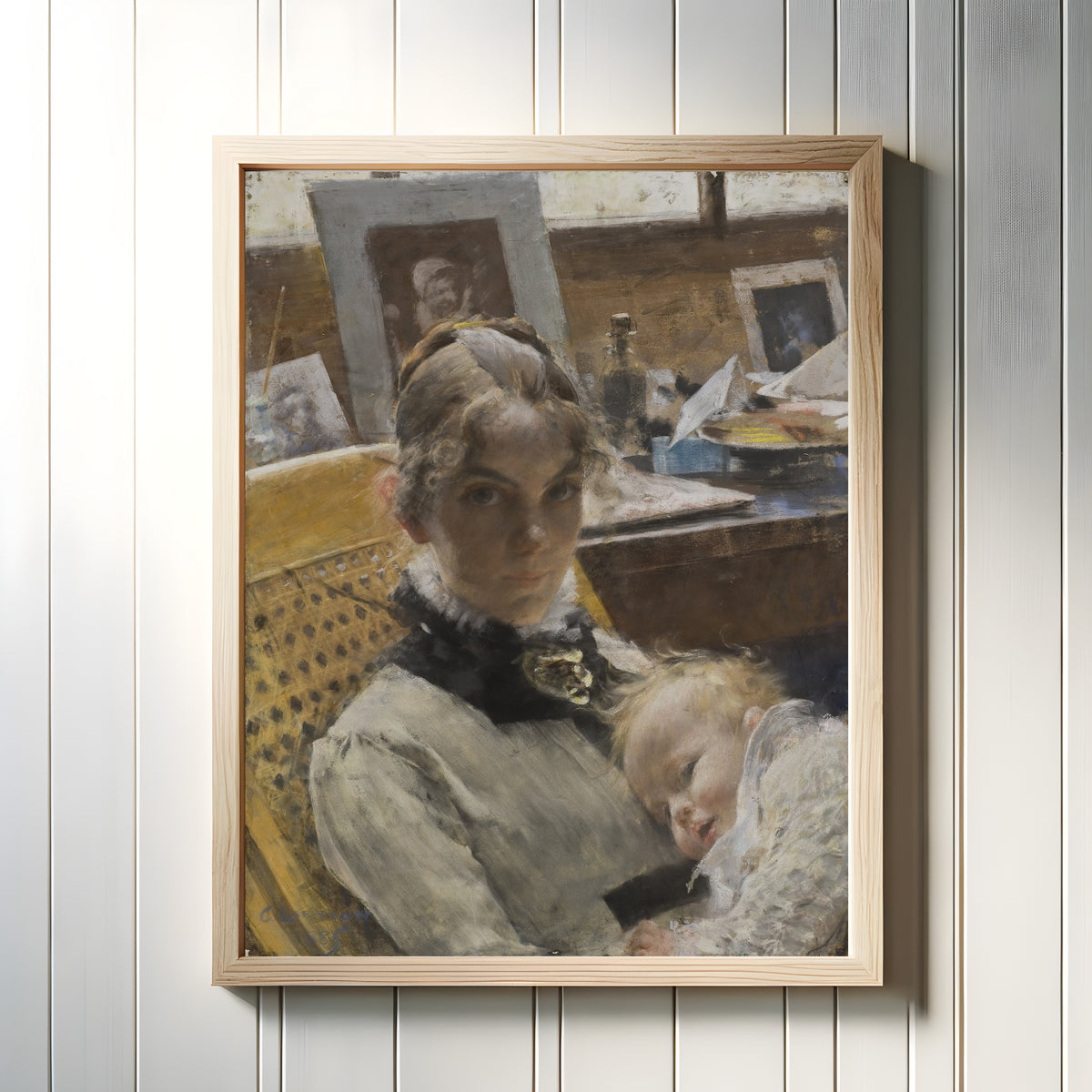 Framed art print of A Studio Idyll. The Artist's Wife and their Daughter by Carl Larsson, in a light wood frame on a white panelled wall