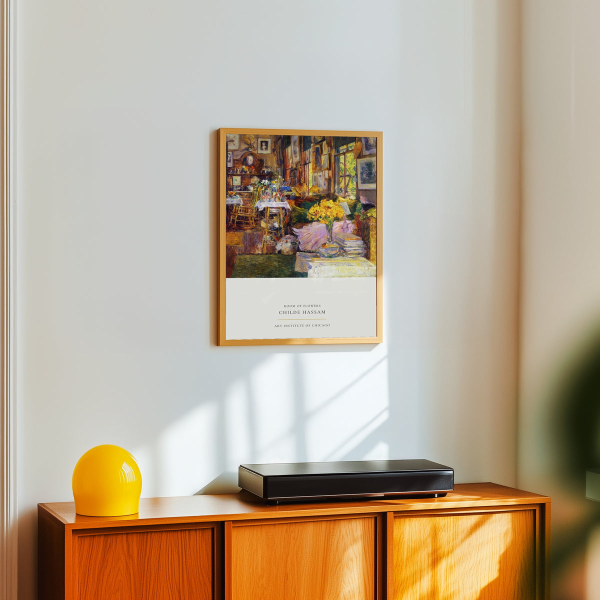 Framed art print of Room of Flowers by Childe Hassam, in a light wood frame on a white wall above an orange sideboard
