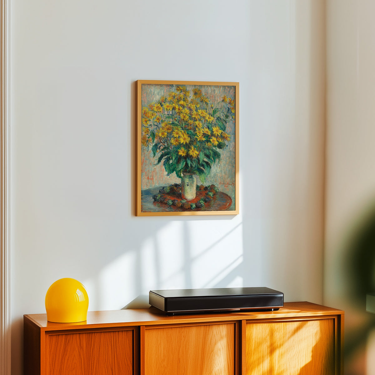 Framed art print of Jerusalem Artichoke Flowers by Claude Monet, in a light wood frame on a white wall above an orange sideboard