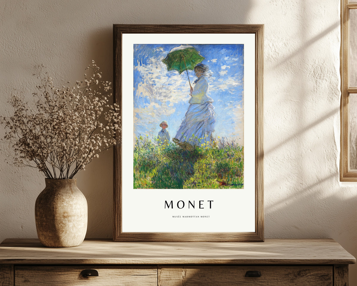 Framed art print of Madame Monet with a Parasol by Claude Monet, in a dark wood frame leaning on a rustic console beside dried flowers