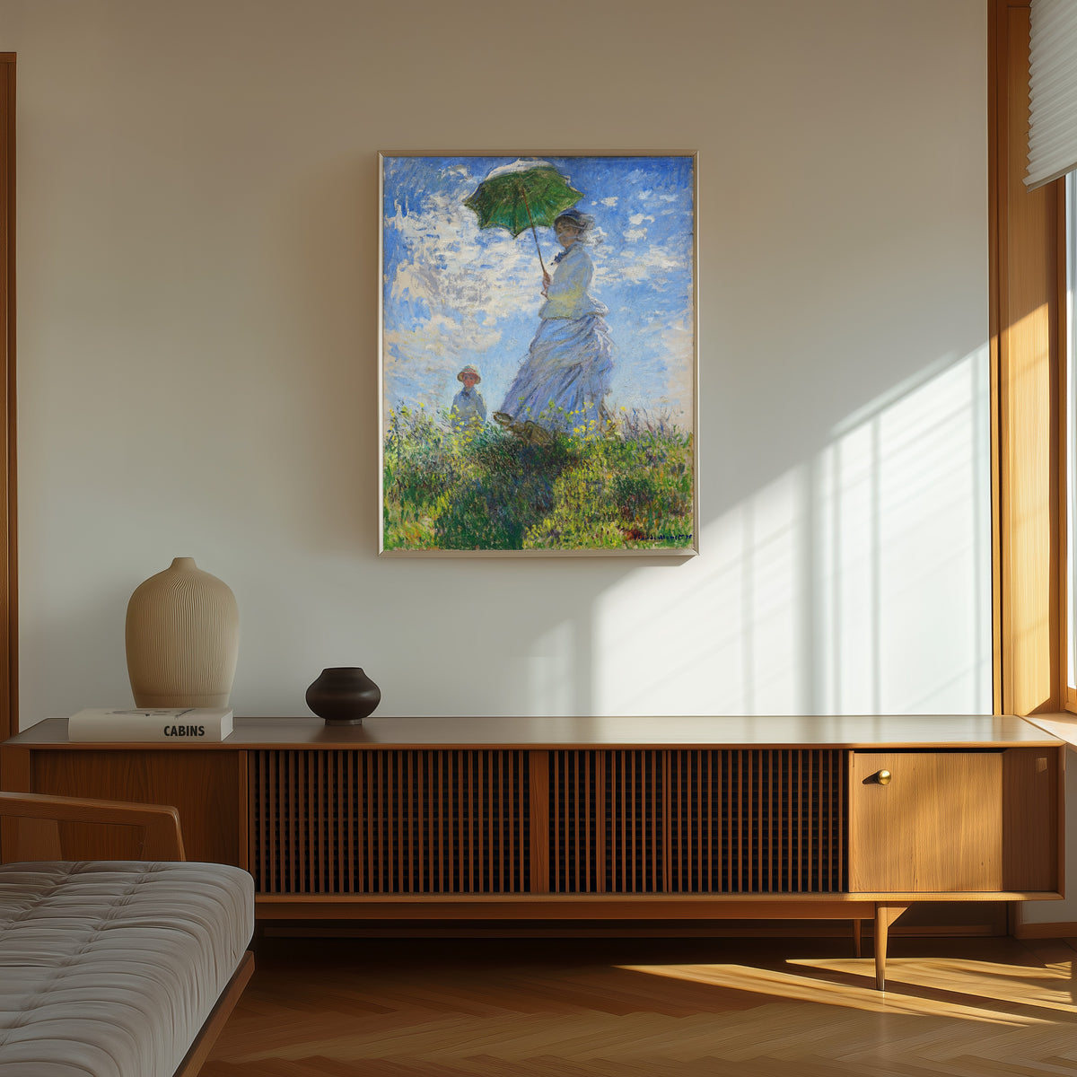 Framed art print of Woman with a Parasol - Madame Monet and Her Son by Claude Monet, in a thin light frame on a sunlit wall above a wooden sideboard