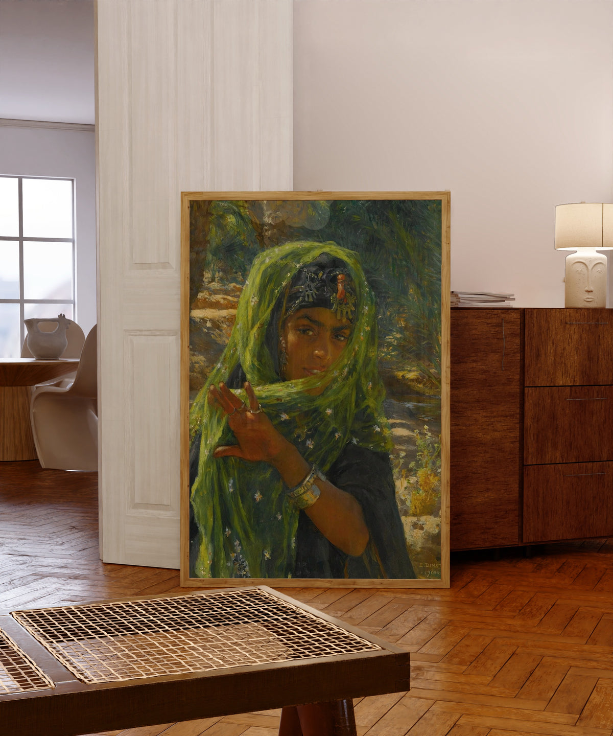 Framed art print of The Girl in the Green Scarf by Nasreddine Dinet, in a light wood frame leaning in a warm room with a parquet floor